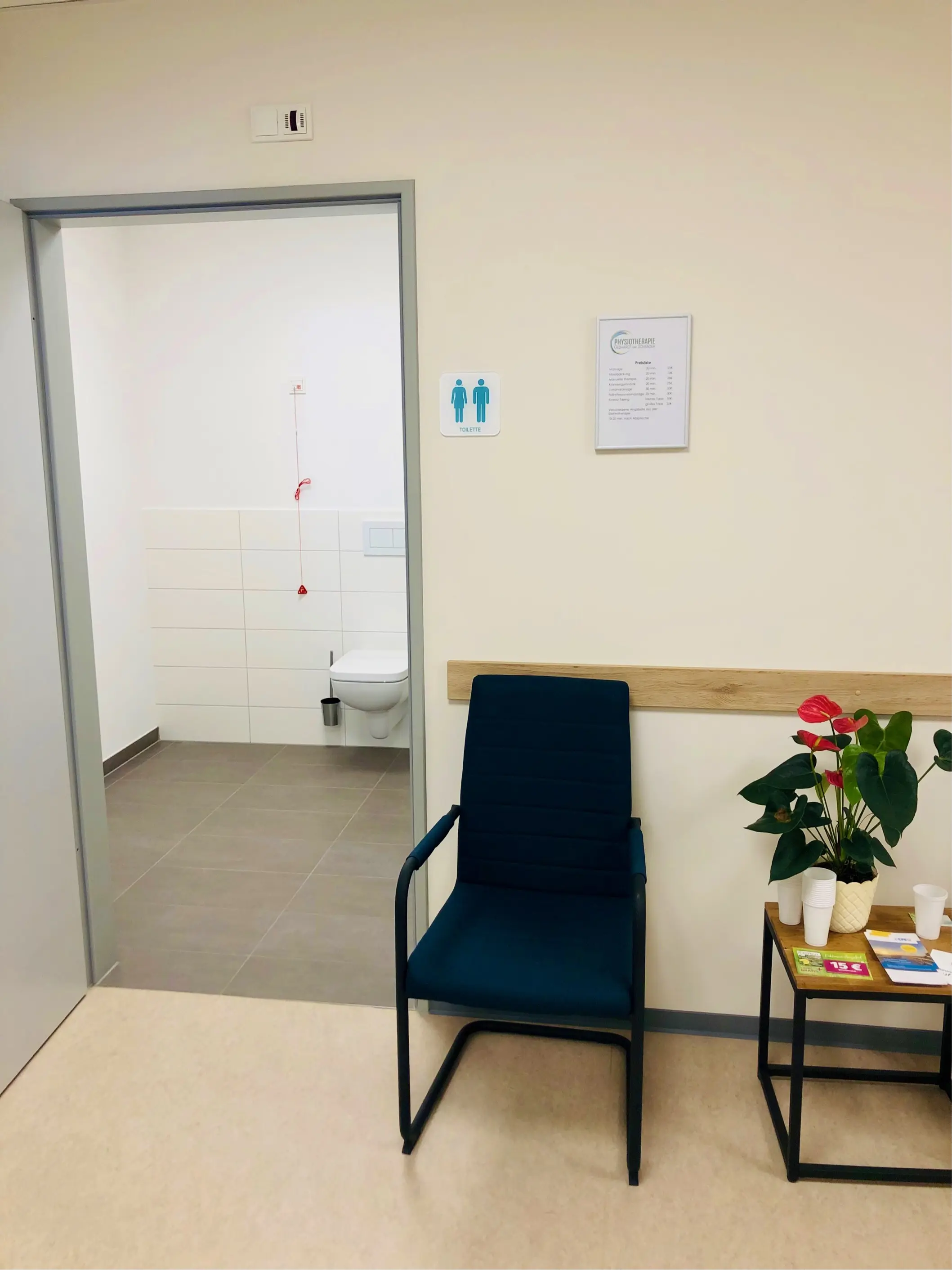 Wartebereich mit blauem Stuhl und Beistelltisch neben dem barrierefreien Toilettenzugang