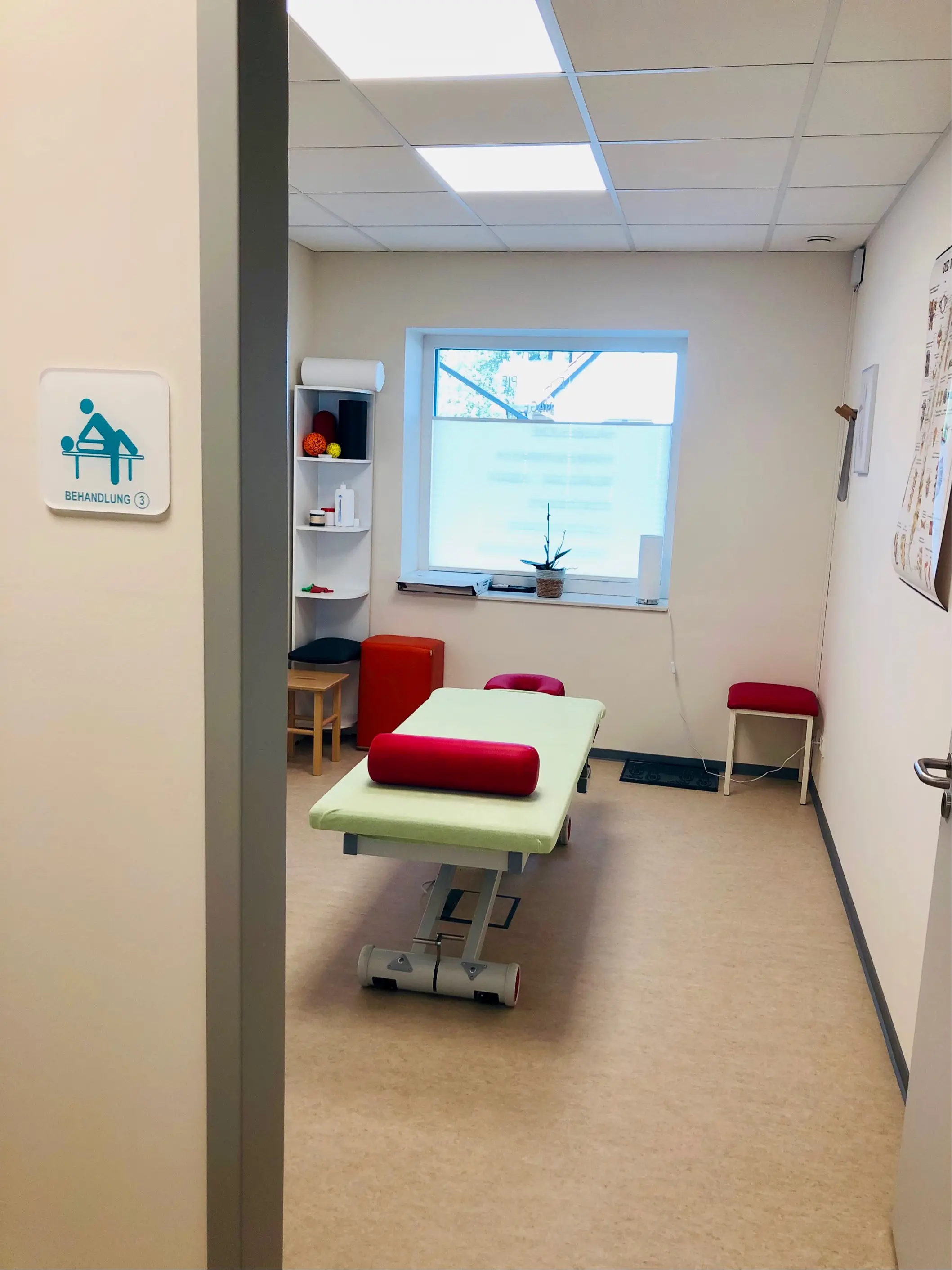 Blick durch die offene Tür in Behandlungsraum 3 mit Therapieliege, Regal und Sitzwürfeln