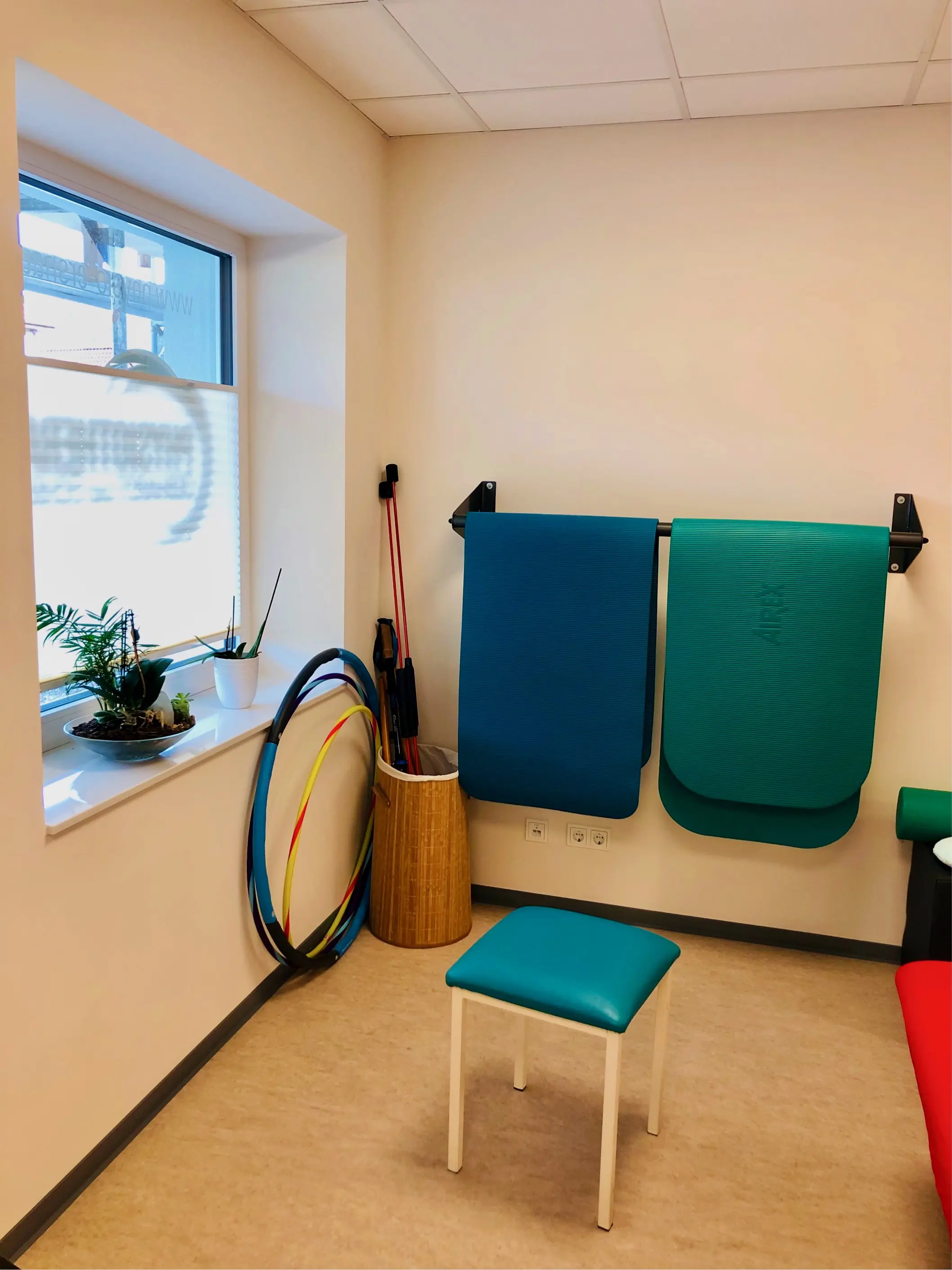 Behandlungsraum mit Gymnastikmatten, Therapiebändern und Hula-Hoop-Reifen an der Wand