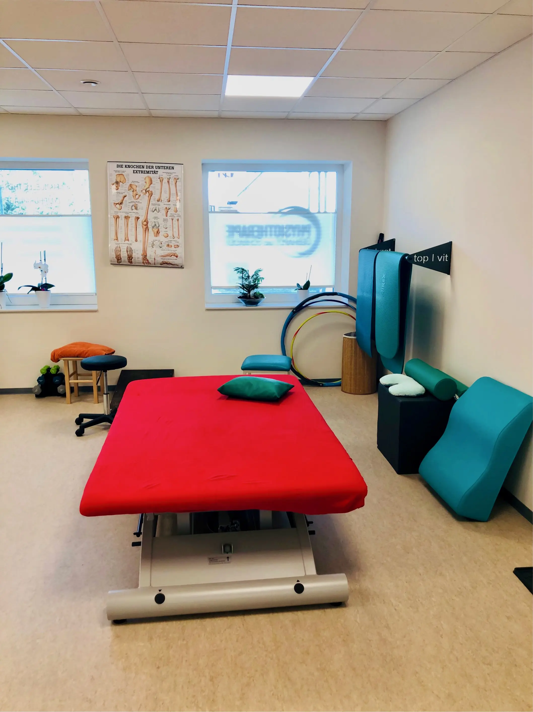 Heller Behandlungsraum mit höhenverstellbarer Therapieliege, anatomischem Poster und Lagerungskissen