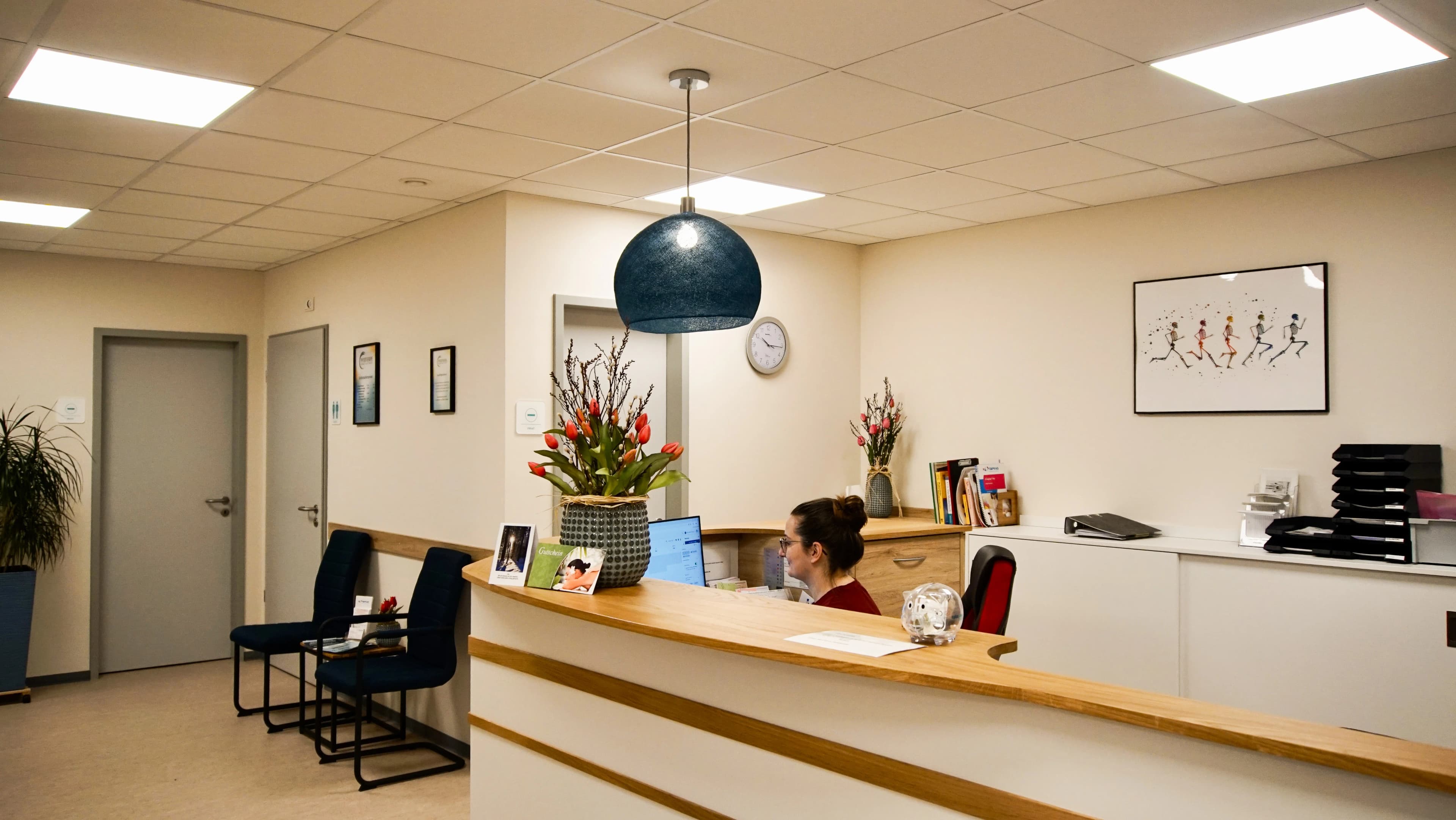Heller Empfangsbereich der Physiotherapie-Praxis mit Holztresen, Pendelleuchte und Blumendekoration